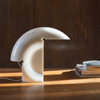 Clérachic resin crescent lamp glowing on a wood table against dark cabinet doors, its cord trailing across the sunlit surface.