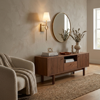 Lit beside a round mirror over a wood console with a vase, this Clérachic wall sconce in brushed brass warms a living room corner.