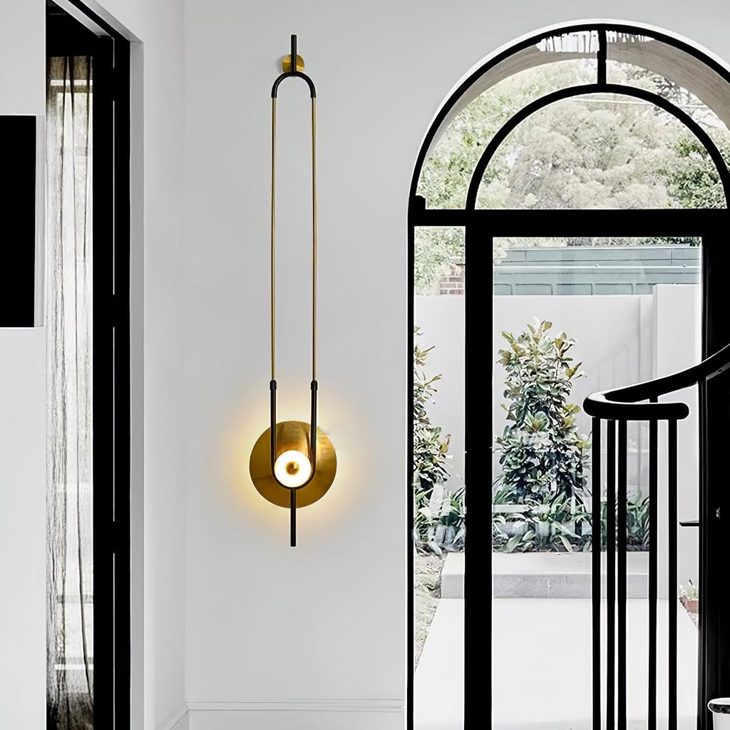 A Clérachic wall light glows beside a black-framed arched doorway, its slim gold loop echoing the hallway's vertical lines.