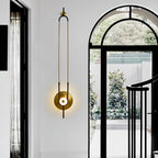 A Clérachic wall light glows beside a black-framed arched doorway, its slim gold loop echoing the hallway's vertical lines.