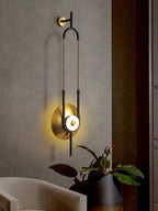 A Clérachic wall sconce glows above a cream armchair and a leafy plant near a maroon-toned doorway.
