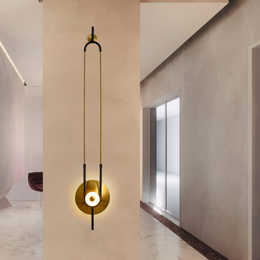 Clérachic's wall sconce is mounted on a warm plaster wall in a hallway, its gold loop stretching above a polished stone floor.
