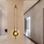 Clérachic's wall sconce is mounted on a warm plaster wall in a hallway, its gold loop stretching above a polished stone floor.