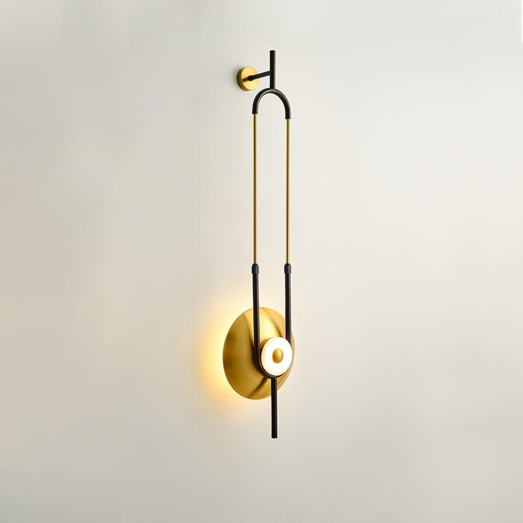 A Clérachic wall sconce is photographed at an angle on an off-white wall, showing the depth of its gold loop in profile.