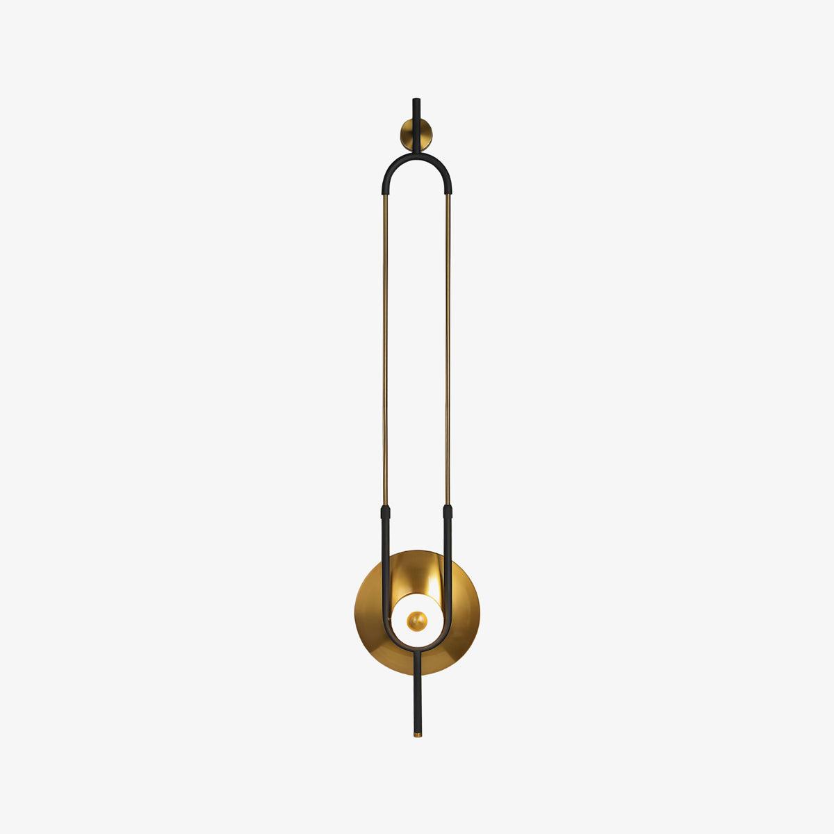 A slim brass loop frame on this Clérachic wall sconce curves down to a round gold disc and a softly lit glass orb, shown alone on a plain backdrop.