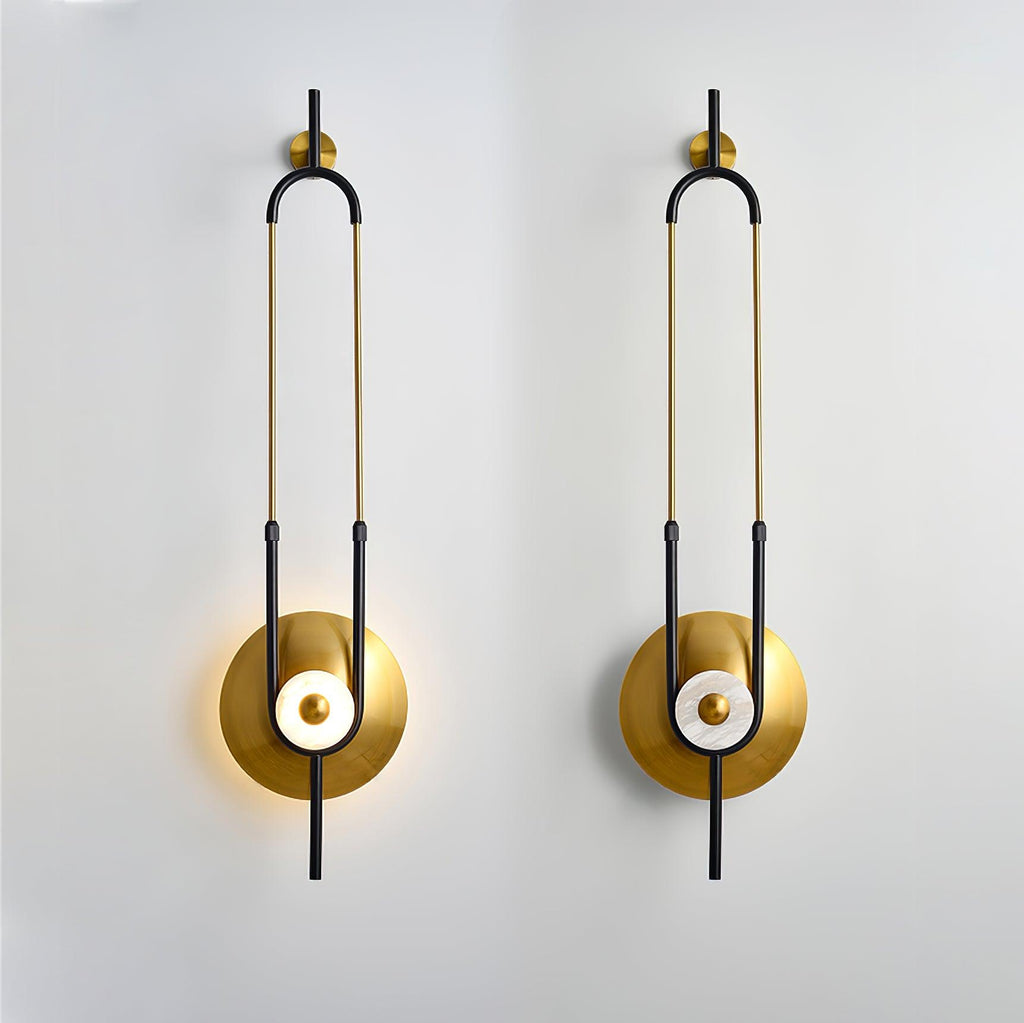 Two Clérachic gold wall sconces are mounted side by side on a plain white wall, each lit at its round base.