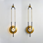 Two Clérachic gold wall sconces are mounted side by side on a plain white wall, each lit at its round base.