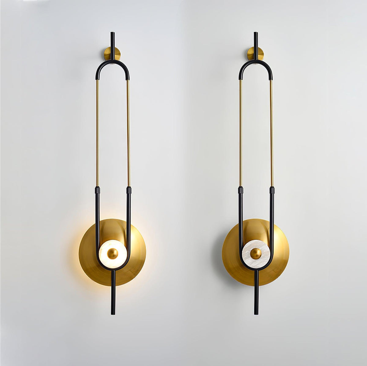 Two Clérachic gold wall sconces are mounted side by side on a plain white wall, each lit at its round base.