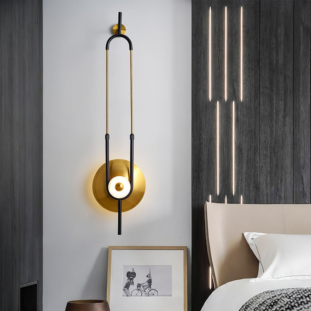 This Clérachic wall light hangs beside a dark accent wall, its slim gold loop echoing a row of vertical pendant lights above the bed.