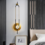 This Clérachic wall light hangs beside a dark accent wall, its slim gold loop echoing a row of vertical pendant lights above the bed.