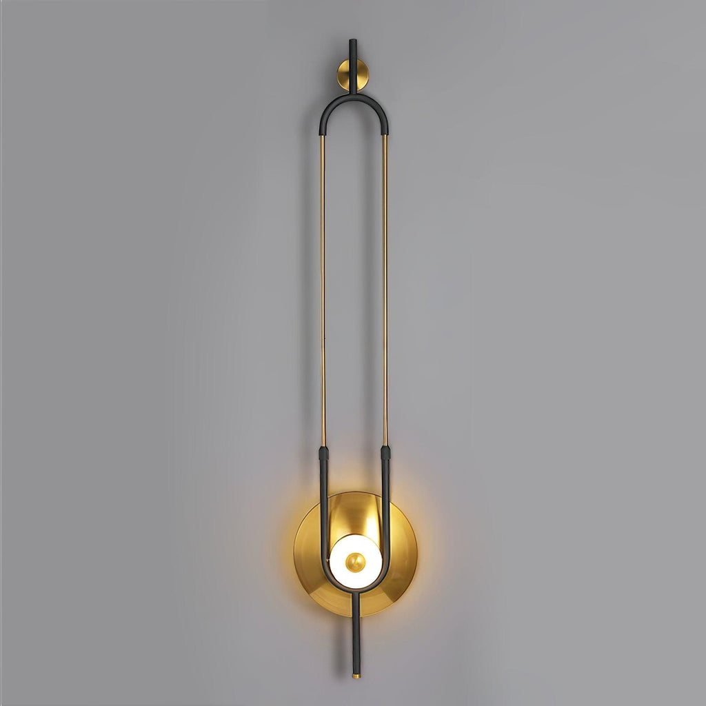 This Clérachic wall sconce is shown full length against a plain grey wall, from its wall bracket to the lit gold base.