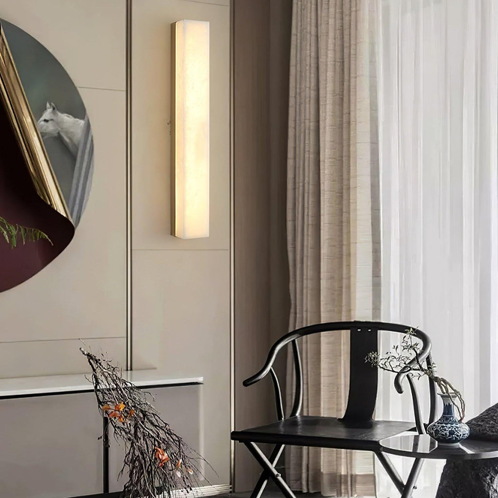 Kristy wall lamp lit on a cream panelled wall beside a round gilt-framed painting and dark chair.