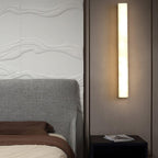 Kristy wall lamp lit on a taupe fabric wall beside a grey upholstered bed and dark nightstand.