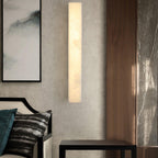 Kristy wall lamp lit above a black side table, framed by walnut panelling and grey marble.