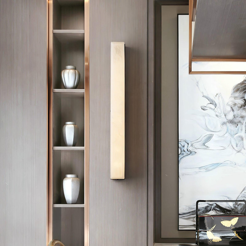 Unlit Kristy wall lamp beside a display niche of silver vases on a grey-brown panelled wall.