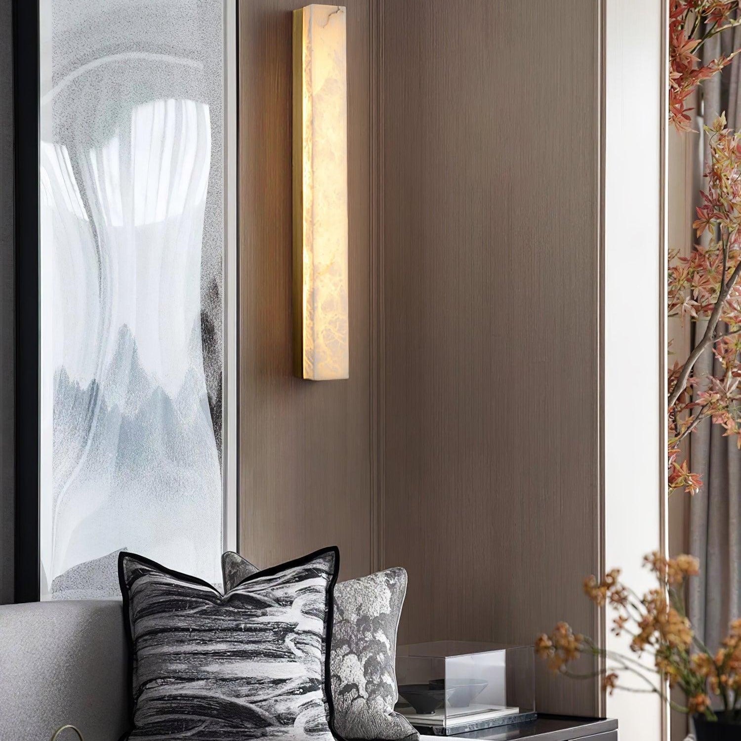 Tight crop of the lit brass Kristy lamp on timber panelling above marbled cushions.