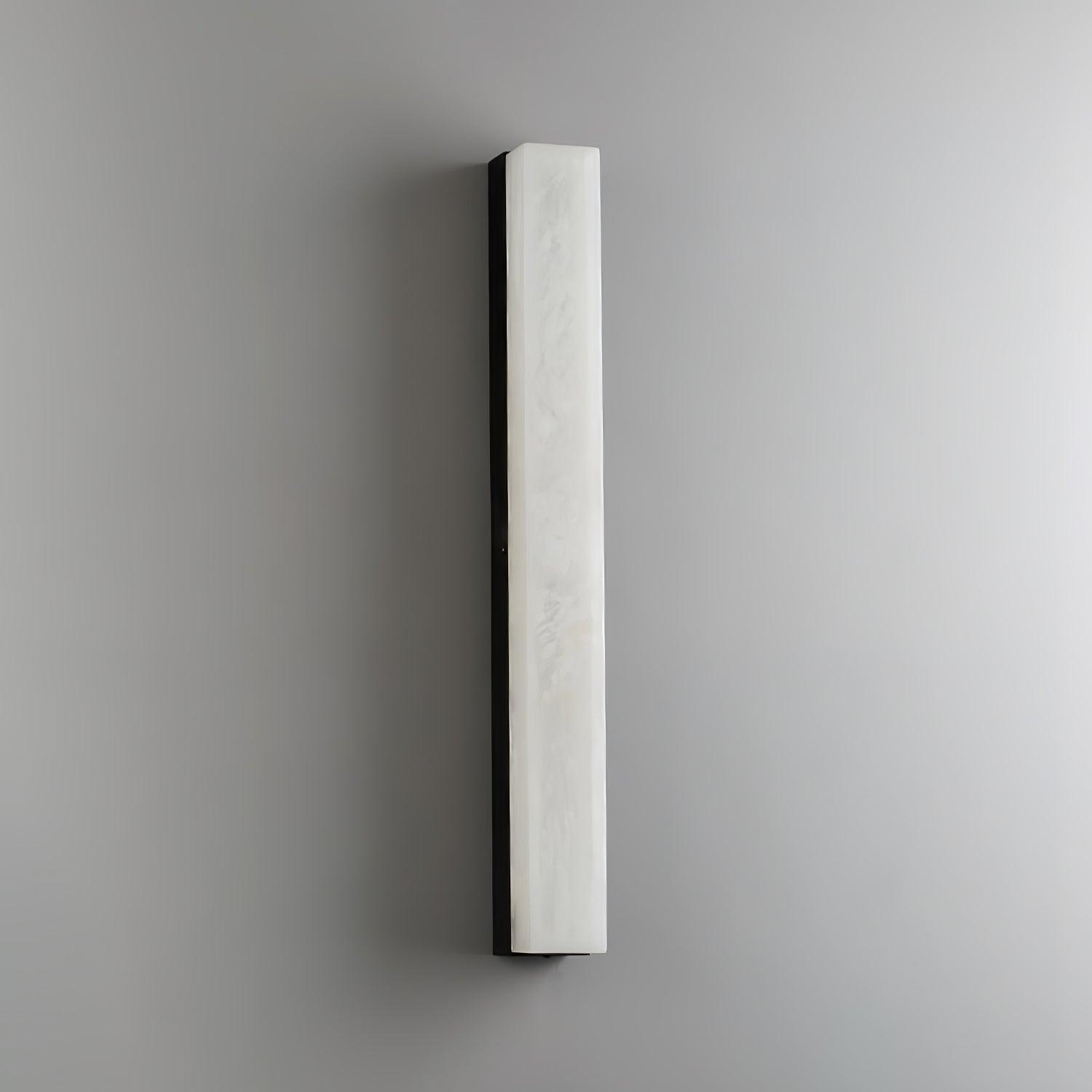 Unlit black-framed Kristy wall lamp on a grey wall, cool white stone face and dark edge.