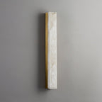 Unlit slim Kristy wall lamp with brass frame on a grey wall, veining across the stone.