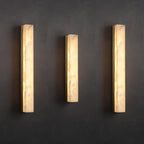 Three lit Kristy wall lamps in different heights mounted side by side on a dark charcoal wall.