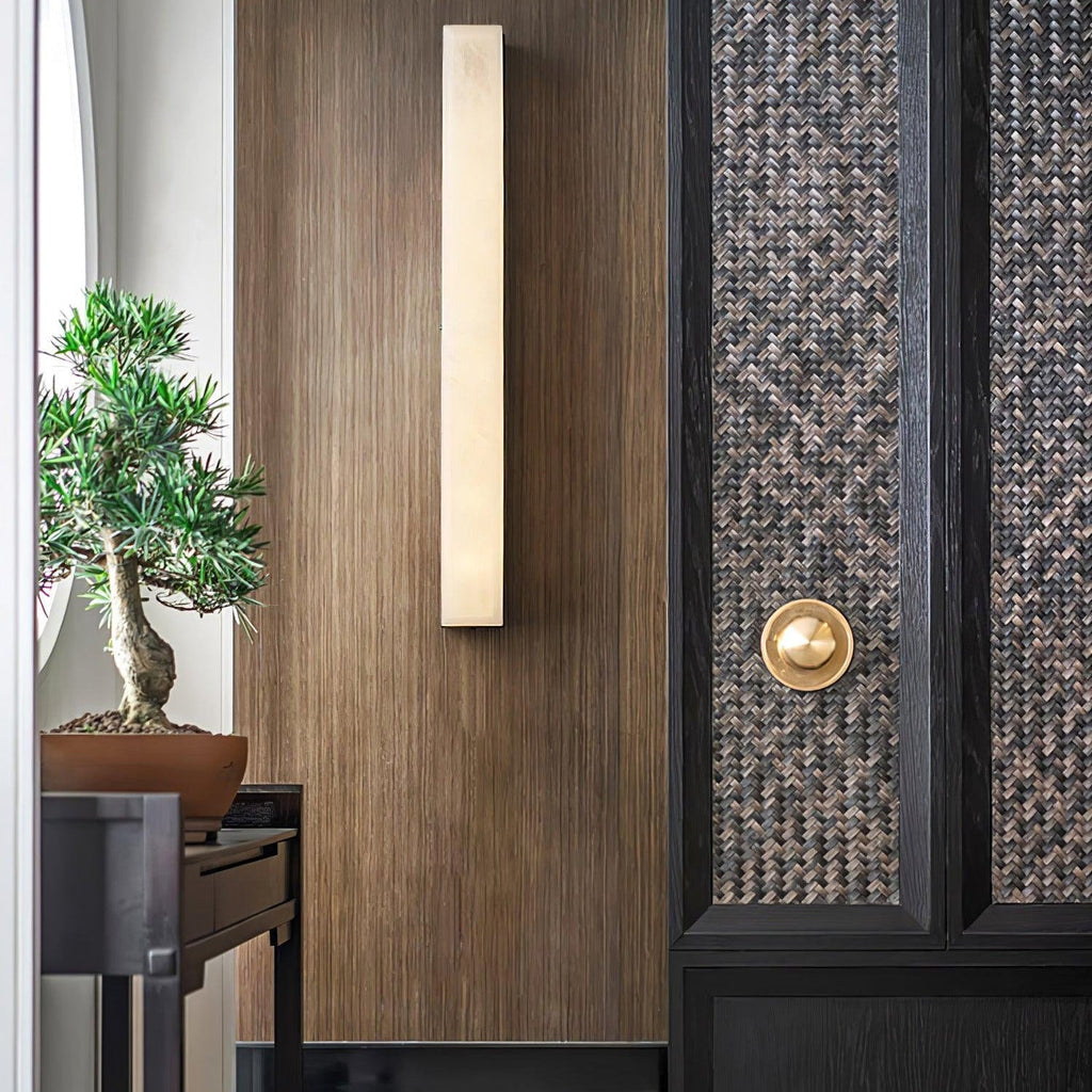 Kristy alabaster wall lamp lit on a walnut panelled entry wall beside a woven cabinet door.