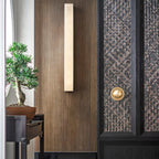 Kristy alabaster wall lamp lit on a walnut panelled entry wall beside a woven cabinet door.