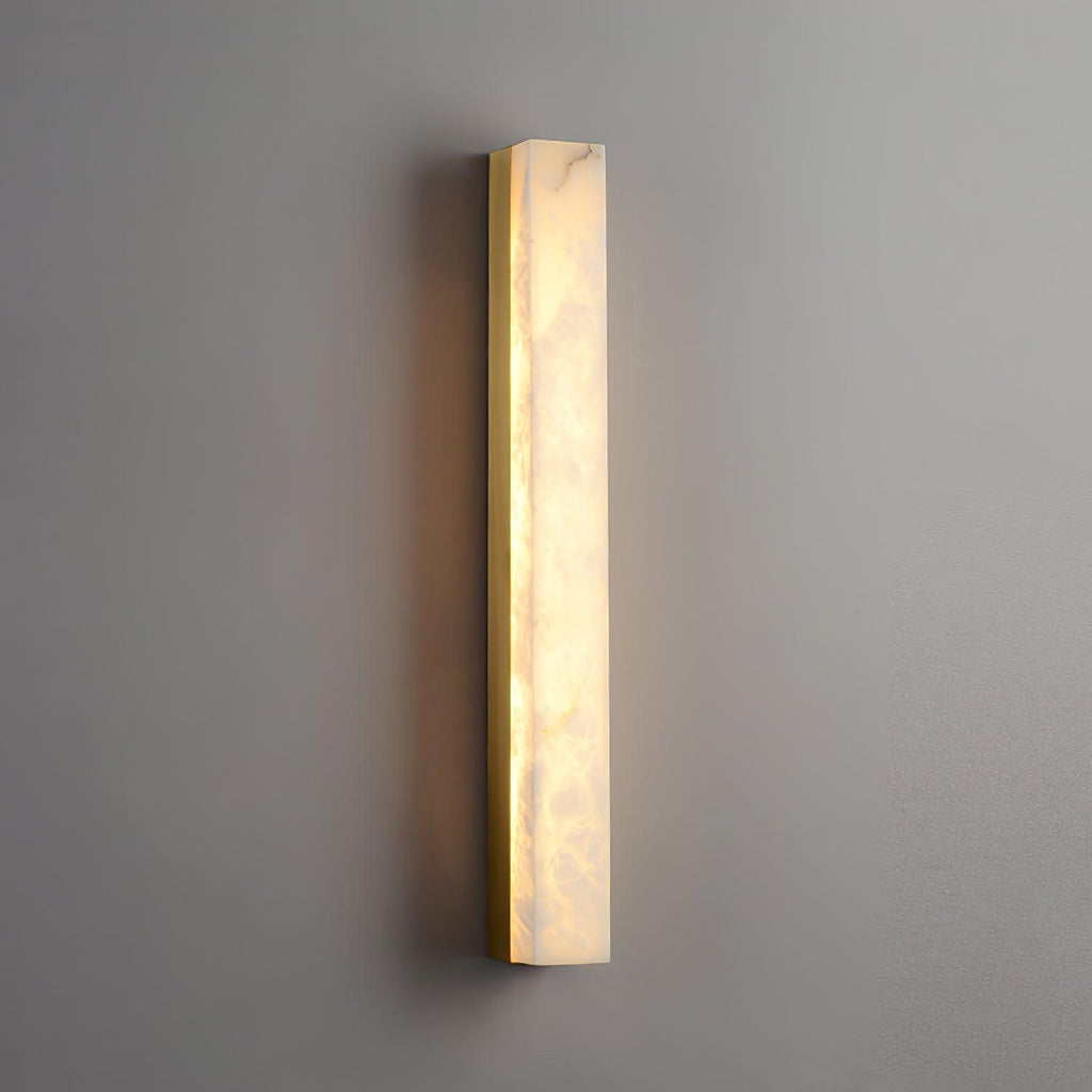 Close angled view of the lit Kristy lamp on a grey wall, brass edge and glow spill visible.