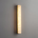 Close angled view of the lit Kristy lamp on a grey wall, brass edge and glow spill visible.