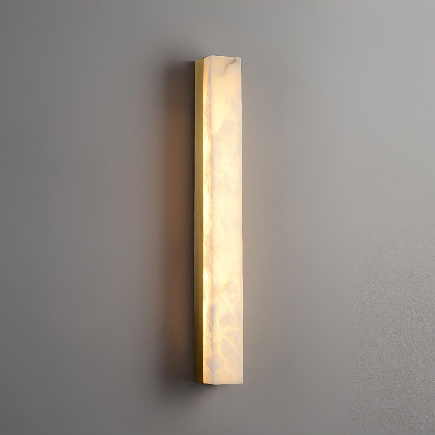 Close angled view of the lit Kristy lamp on a grey wall, brass edge and glow spill visible.