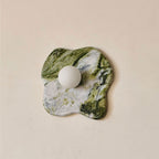 Unlit against a plain beige wall, this Clérachic wall light's green-and-white marble takes on an irregular, puddle-like outline.