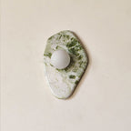 A more angular, diamond-shaped cut of green-and-white marble forms this Clérachic wall light, shown unlit on a beige wall.