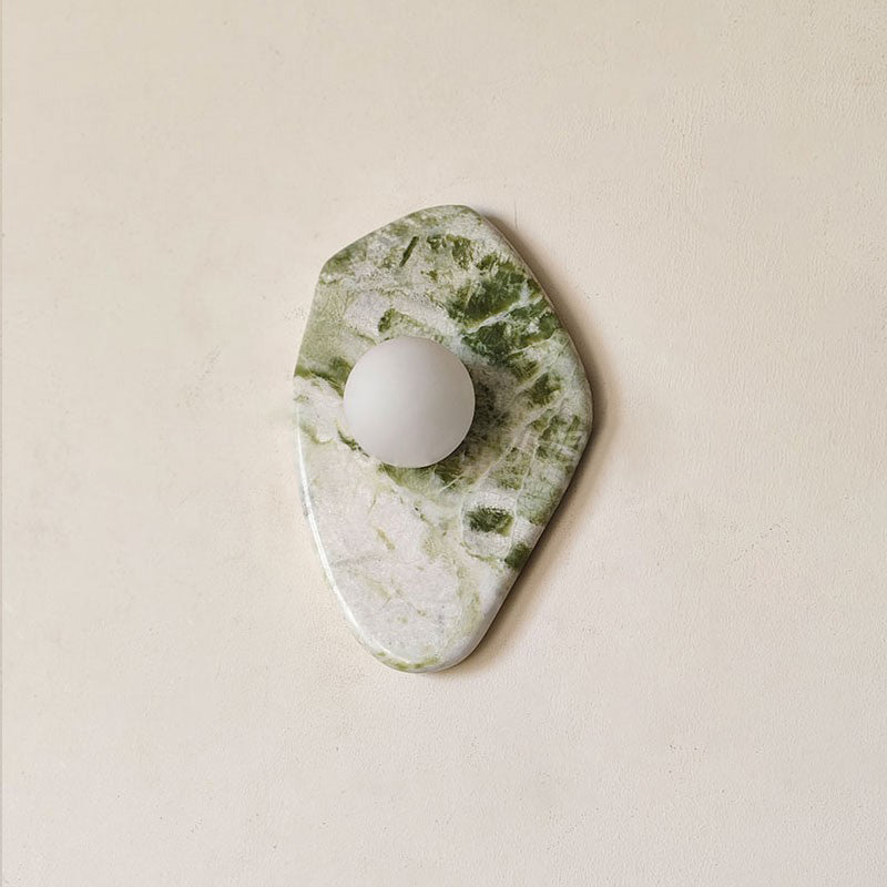 A more angular, diamond-shaped cut of green-and-white marble forms this Clérachic wall light, shown unlit on a beige wall.