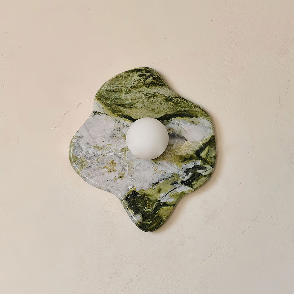 This Clérachic wall light's freeform marble slab spans wider than tall, its frosted glass globe set toward one edge.