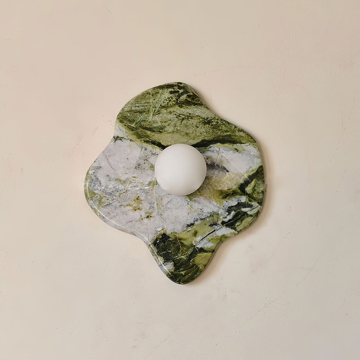 This Clérachic wall light's freeform marble slab spans wider than tall, its frosted glass globe set toward one edge.