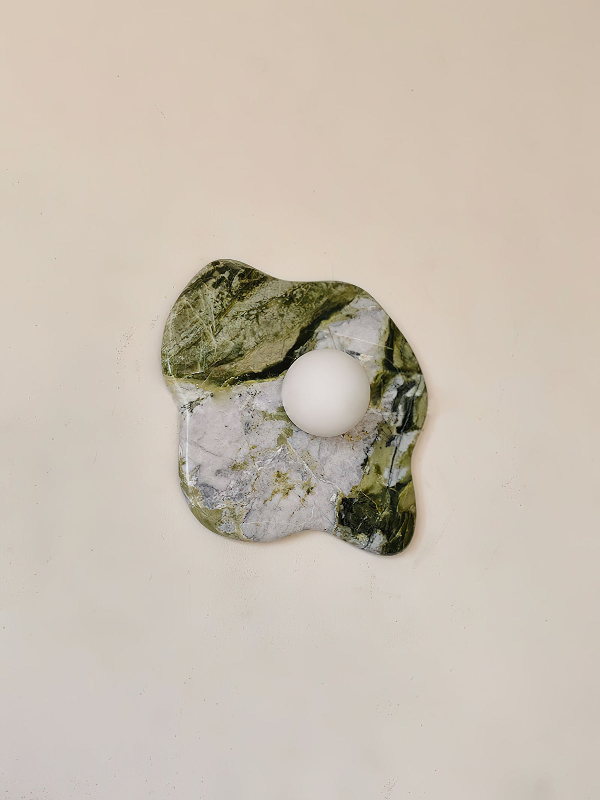 A tightly cropped view of this Clérachic wall light shows striped green marble meeting white stone within the same slab.