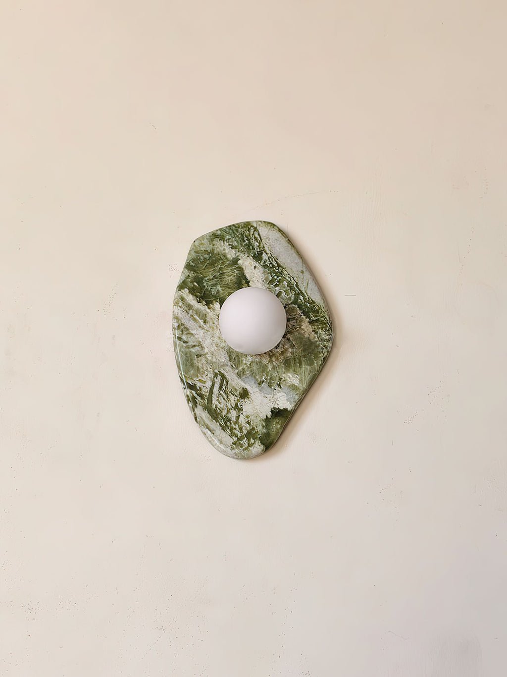 Shown in a narrow vertical crop, the diamond-cut marble of this Clérachic wall light stands unlit against a beige wall.
