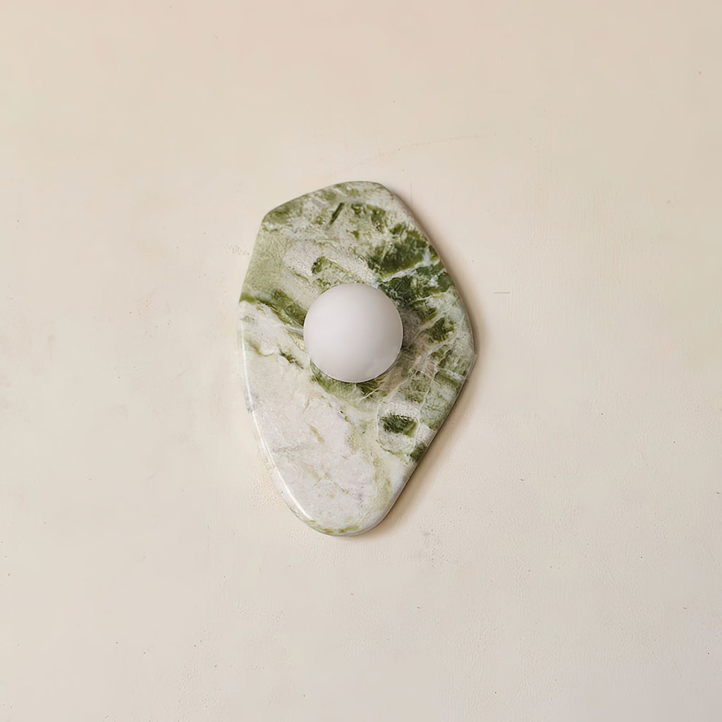 This angled view of the Clérachic wall light shows its diamond marble slab with the frosted globe set near the centre.