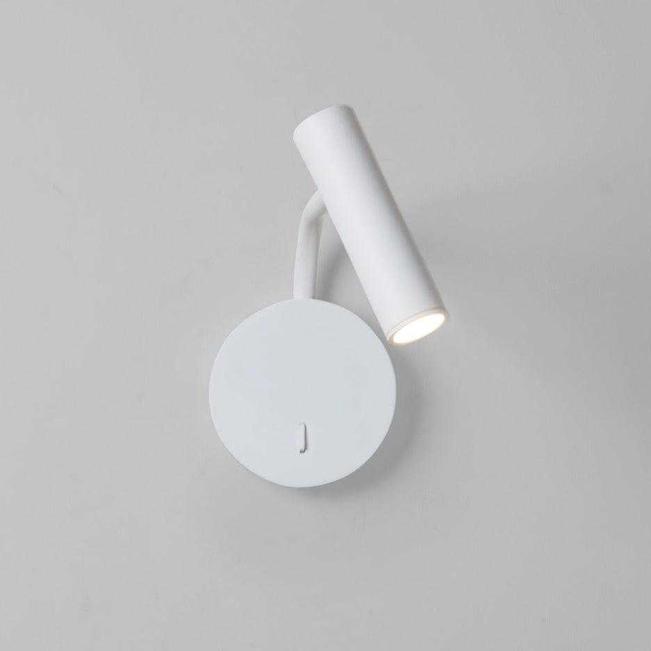 A white Clérachic wall sconce with its arm curved down, lit against a plain grey backdrop.