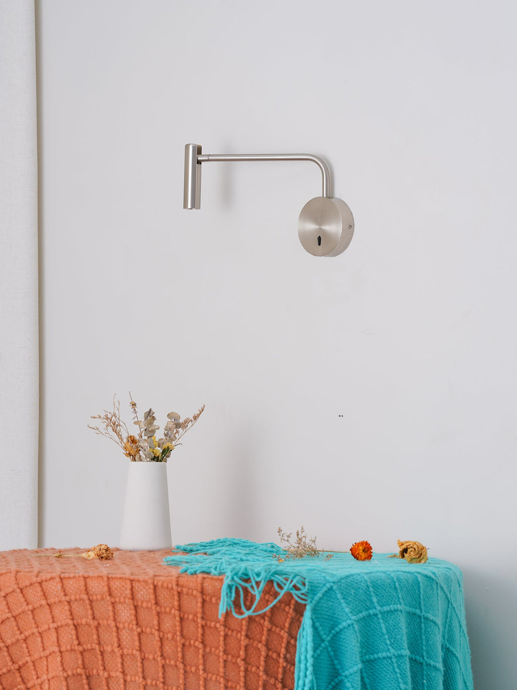 This sand nickel Clérachic wall sconce sits above a styled bench, its arm reaching outward.