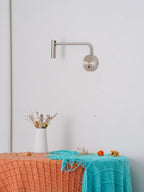 This sand nickel Clérachic wall sconce sits above a styled bench, its arm reaching outward.