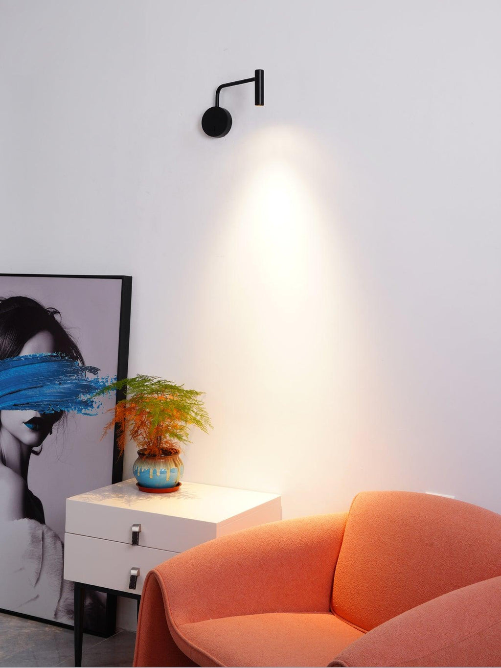 This black Clérachic wall sconce throws a warm beam above a styled dresser and armchair corner.
