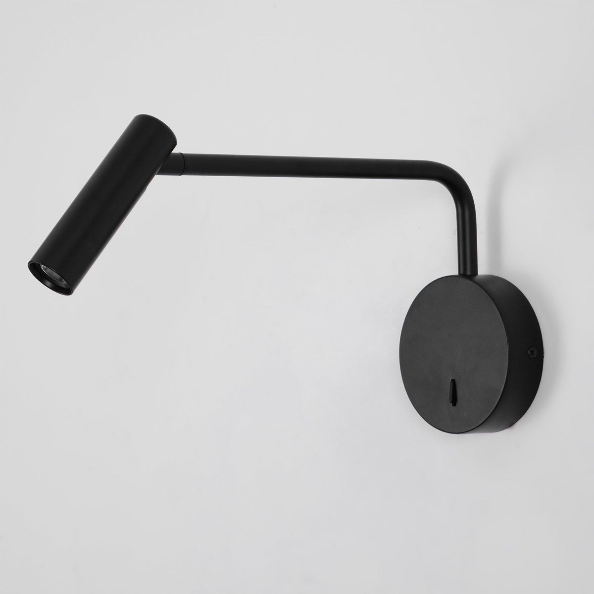 With its arm bent low, this black Clérachic wall sconce directs a warm beam down a grey backdrop.