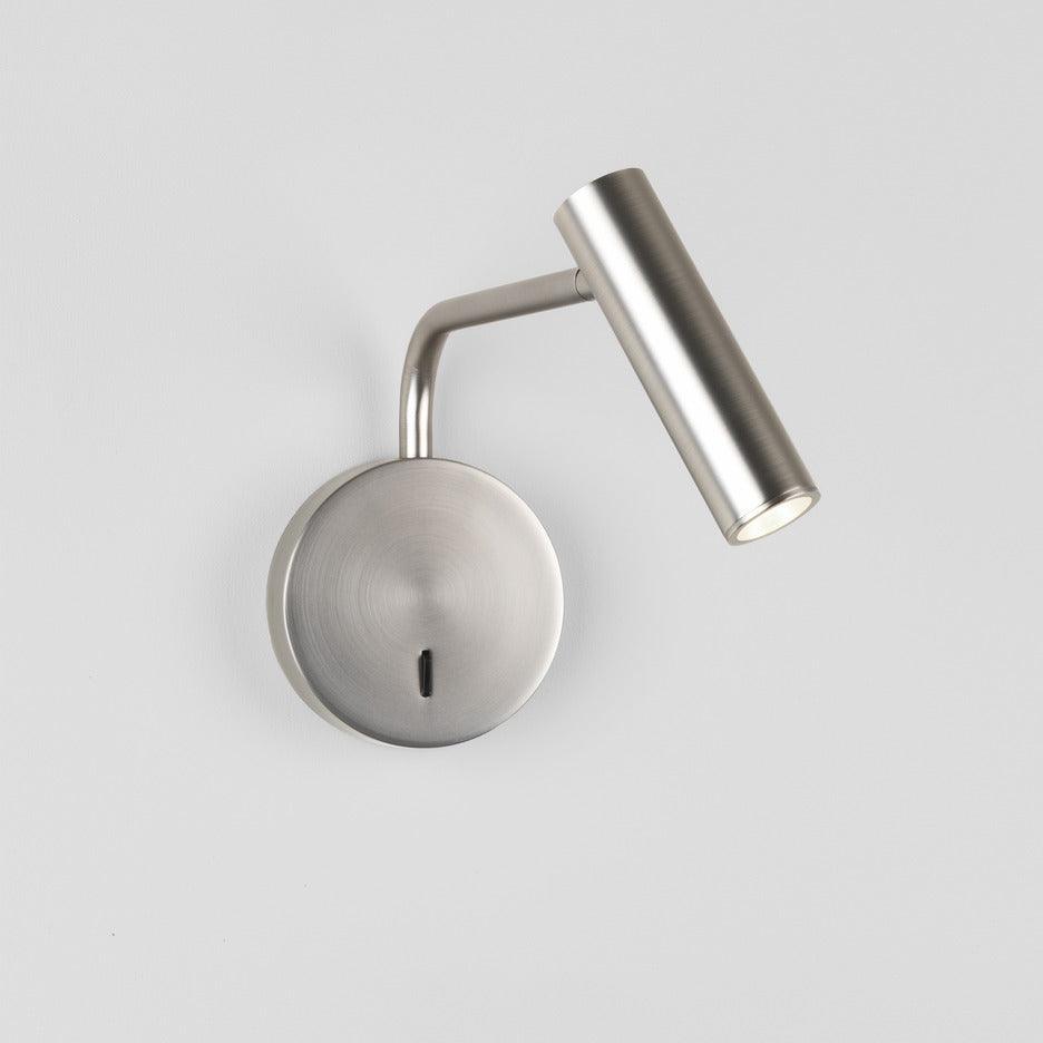 A sand nickel Clérachic wall sconce with its head tilted upward, photographed on a white background.