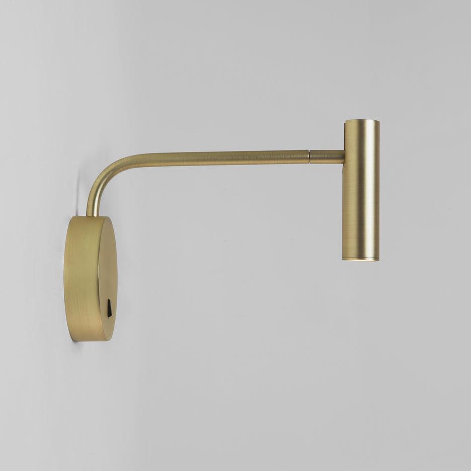 Unlit against a plain grey backdrop, this gold Clérachic wall sconce shows its long arm and disc base.