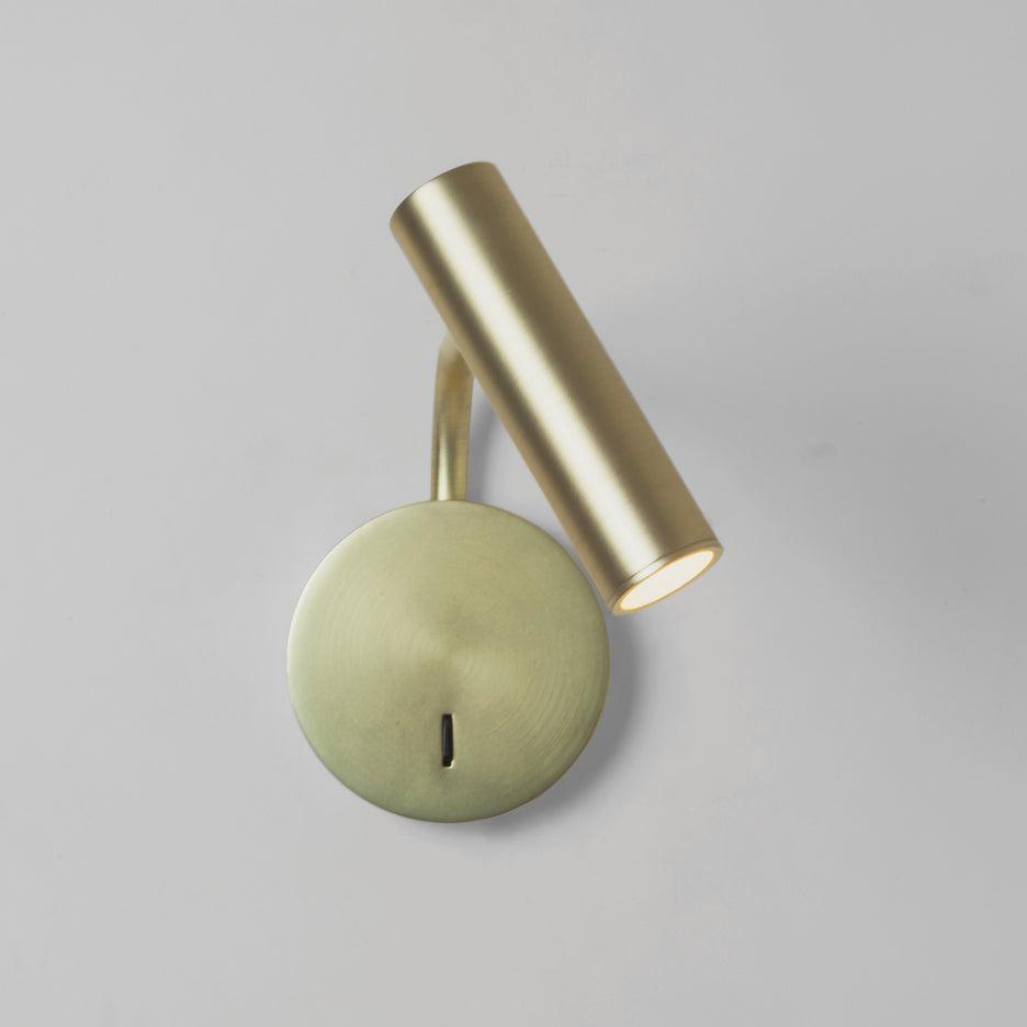 A gold Clérachic wall sconce with its head angled forward, photographed on a plain backdrop.