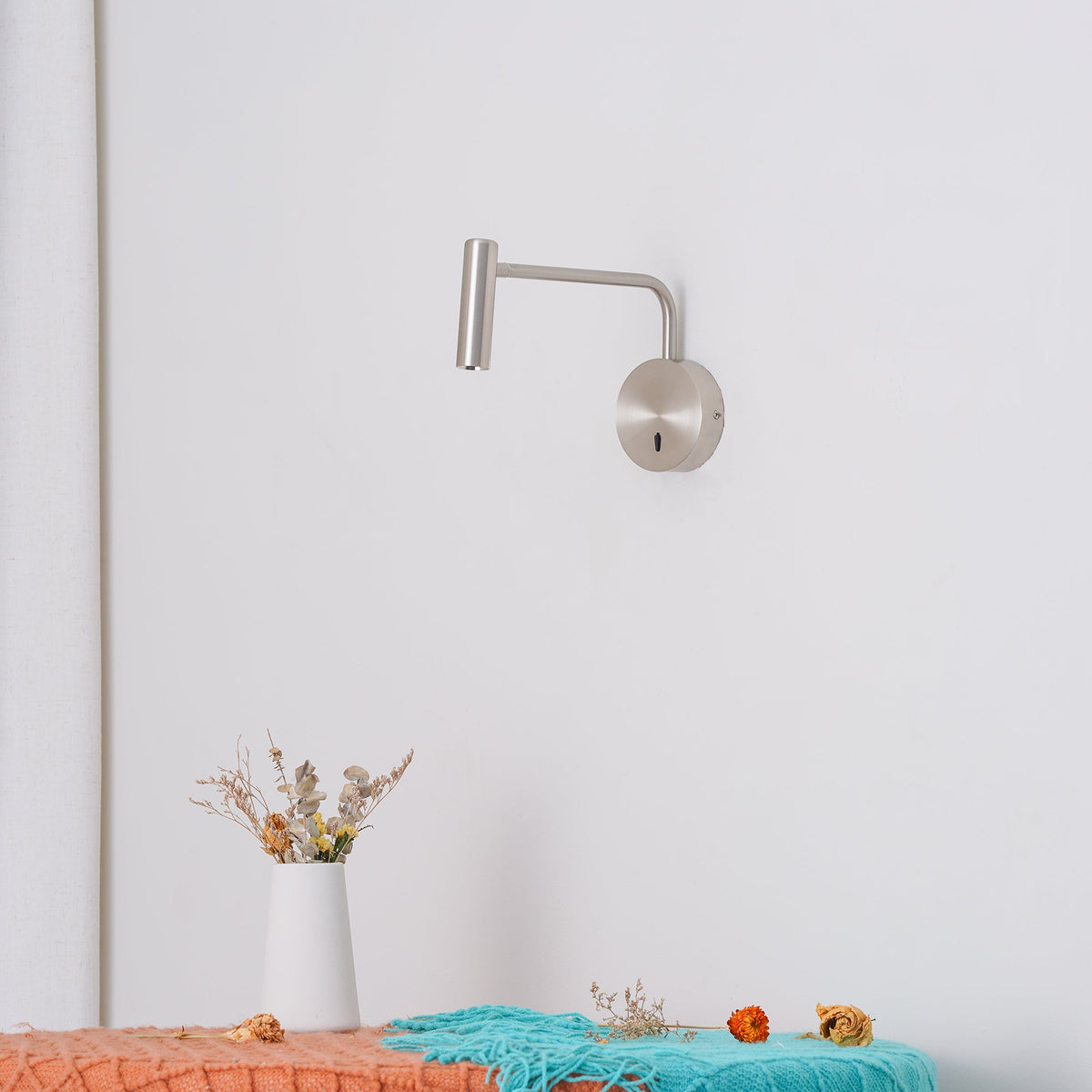 Above a bench styled with dried flowers, this sand nickel Clérachic wall sconce reaches out from the wall.