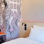 A black Clérachic wall sconce mounted on a wood headboard beside an illustrated mural wall.