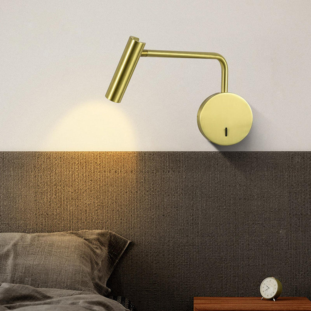 A gold Clérachic wall sconce glows above a dark headboard beside a bedside clock.