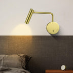 A gold Clérachic wall sconce glows above a dark headboard beside a bedside clock.