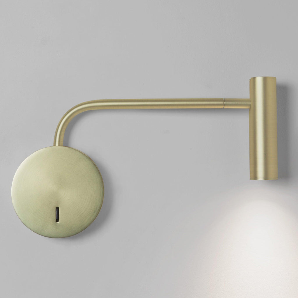 With a long arm casting light downward, this gold Clérachic wall sconce is shown on a grey backdrop.