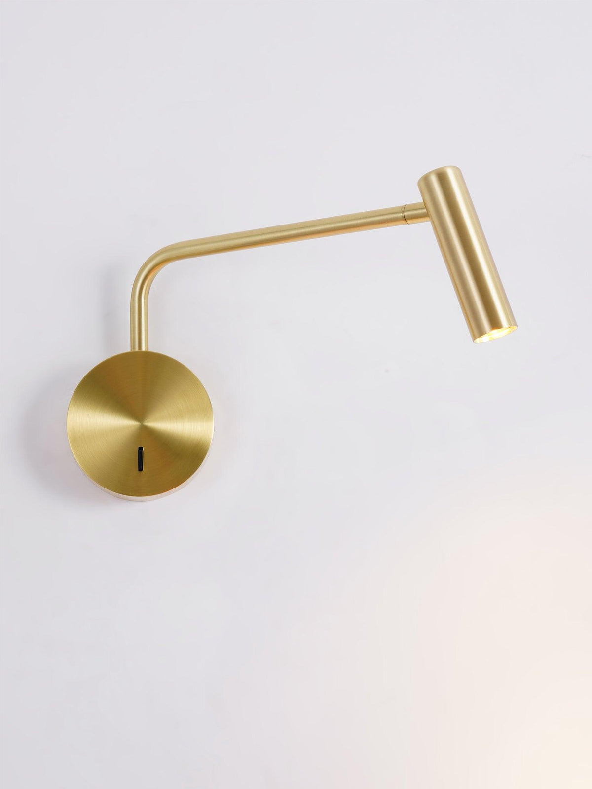 A gold Clérachic wall sconce with its arm bent low, photographed against an off-white backdrop.